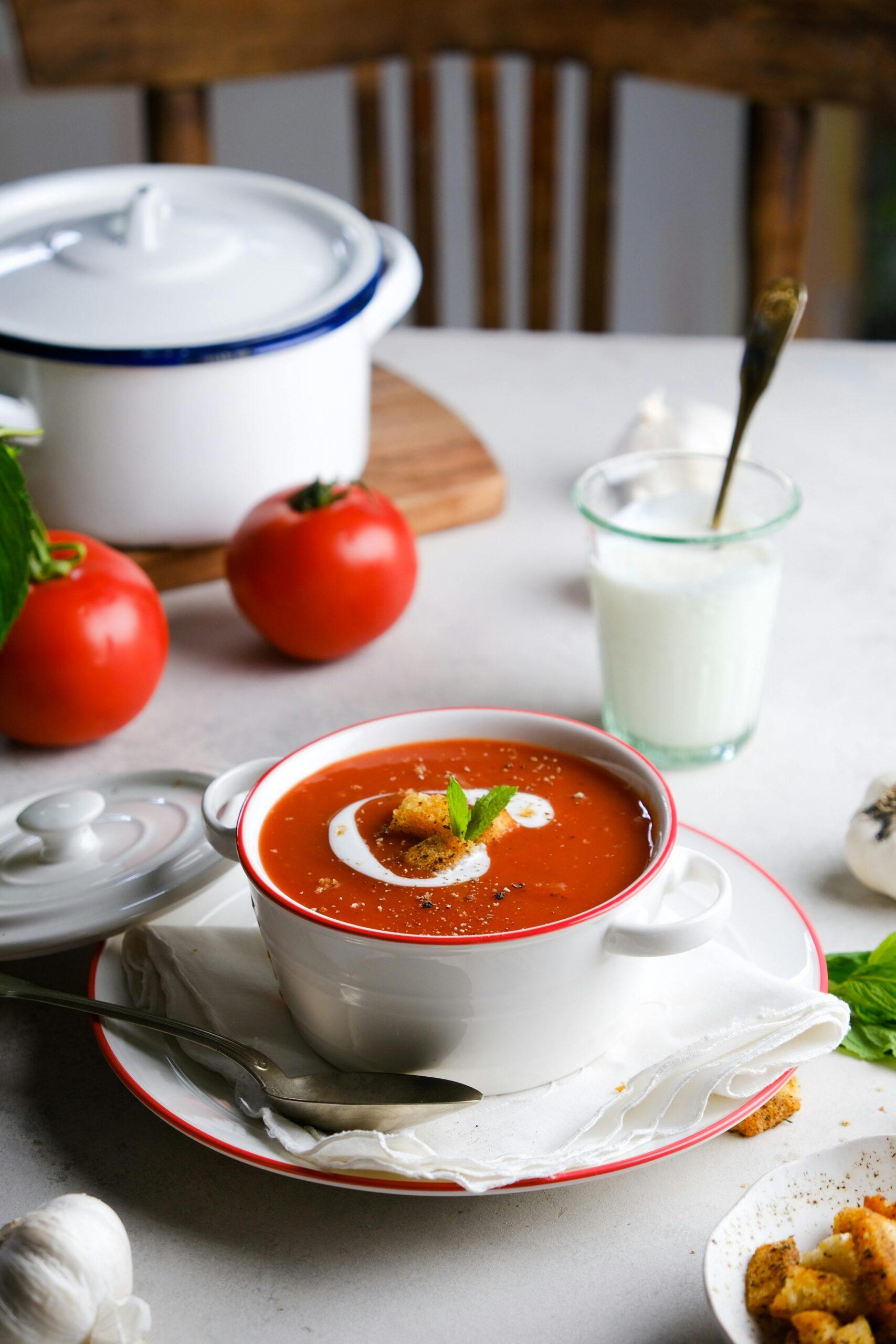 A vibrant bowl of homemade tomato soup garnished with croutons and cream, ideal for food lovers.