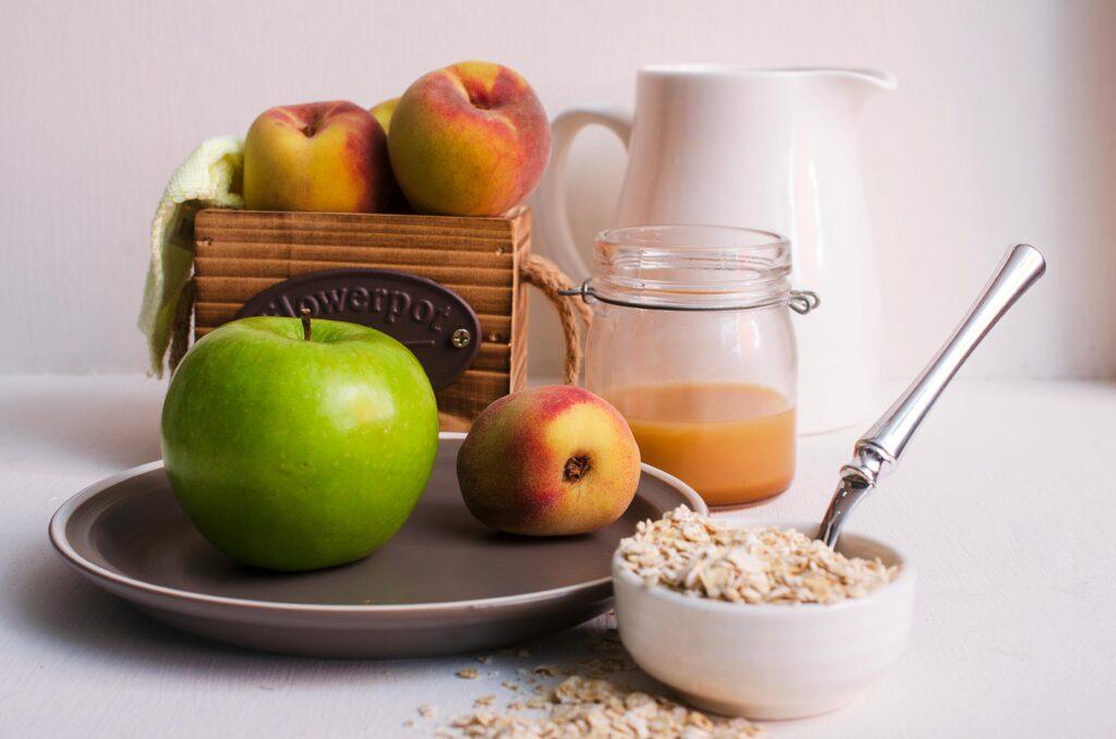 Still life of fresh green apple, peaches, and oats in a cozy kitchen setting.