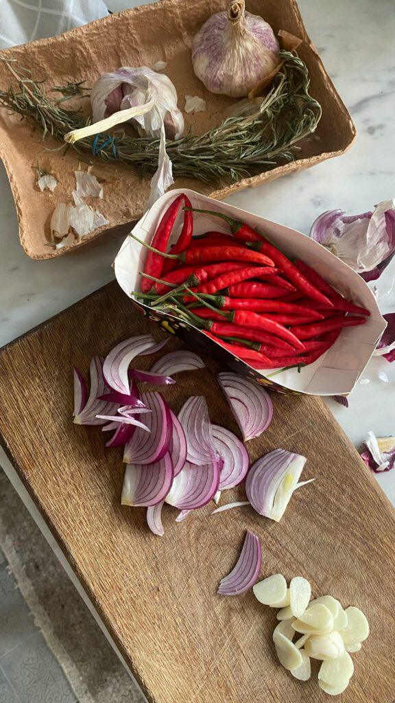 Overhead view of chilies, onions, garlic, and rosemary on a cooking board, perfect for culinary inspiration.