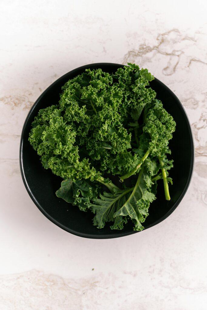 Top view of fresh kale leaves in a black bowl against a marble background. Perfect for healthy eating visuals.