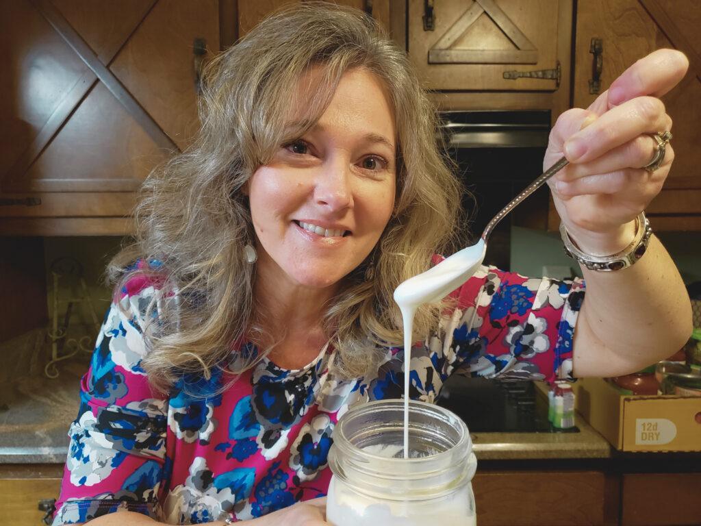 A mid-life woman holding a spoon filled with thick, gut-healthy milk kefir