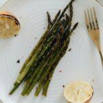 Delicious roasted asparagus served on a ceramic plate with grilled lemon and fork for a healthy meal.